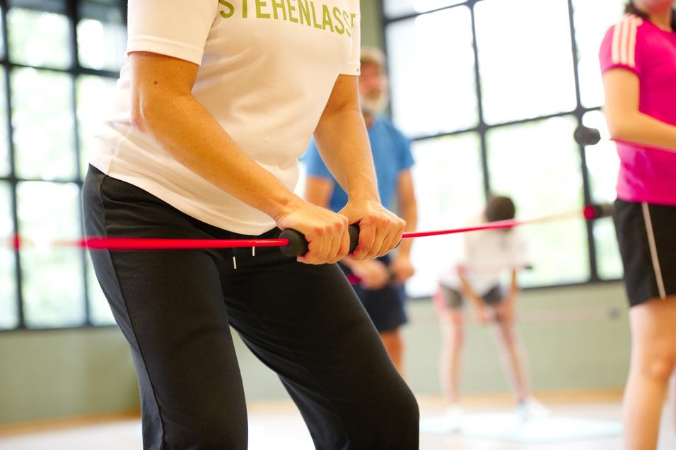 Nahaufnahme einer Person mit einem Widerstandsband im Fitnessstudio, umgeben von weiteren trainierenden Personen.